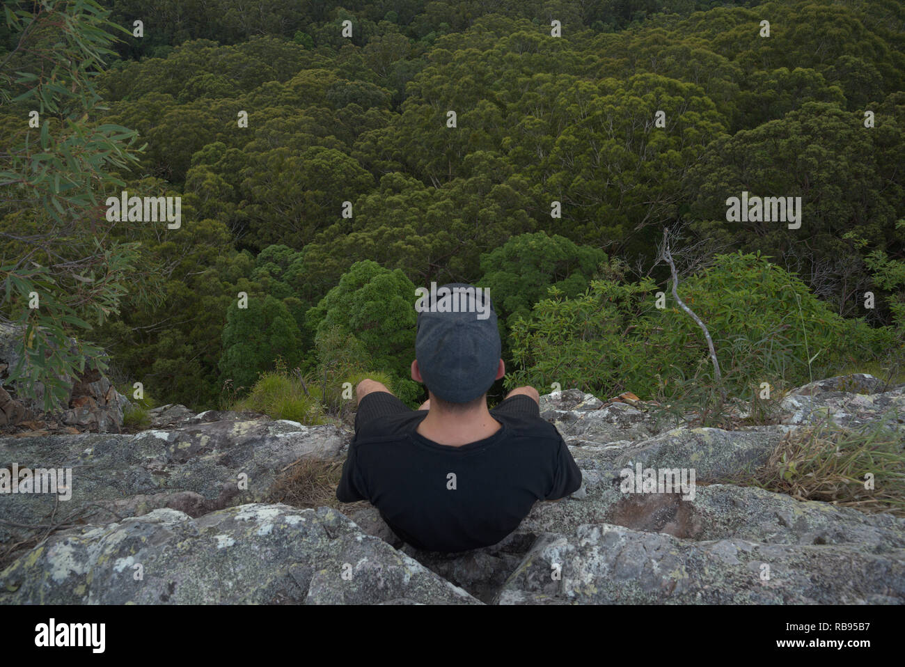 Mann sitzt auf der Kante einer Klippe auf einem Wald Stockfoto