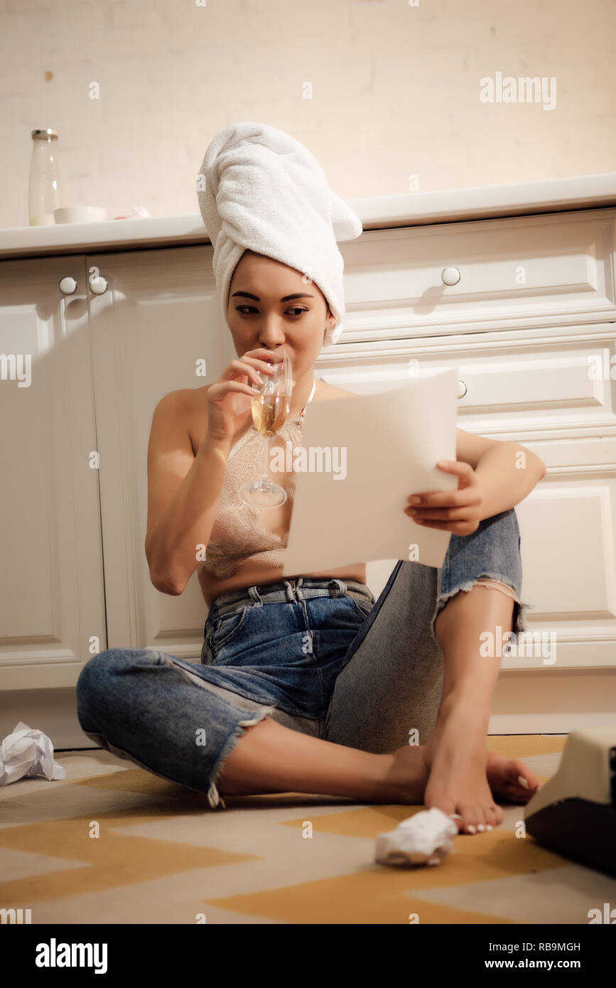 Schöne junge Frau mit Handtuch auf dem Kopf, Wein trinken und Lesen von Papier zu Hause Stockfoto