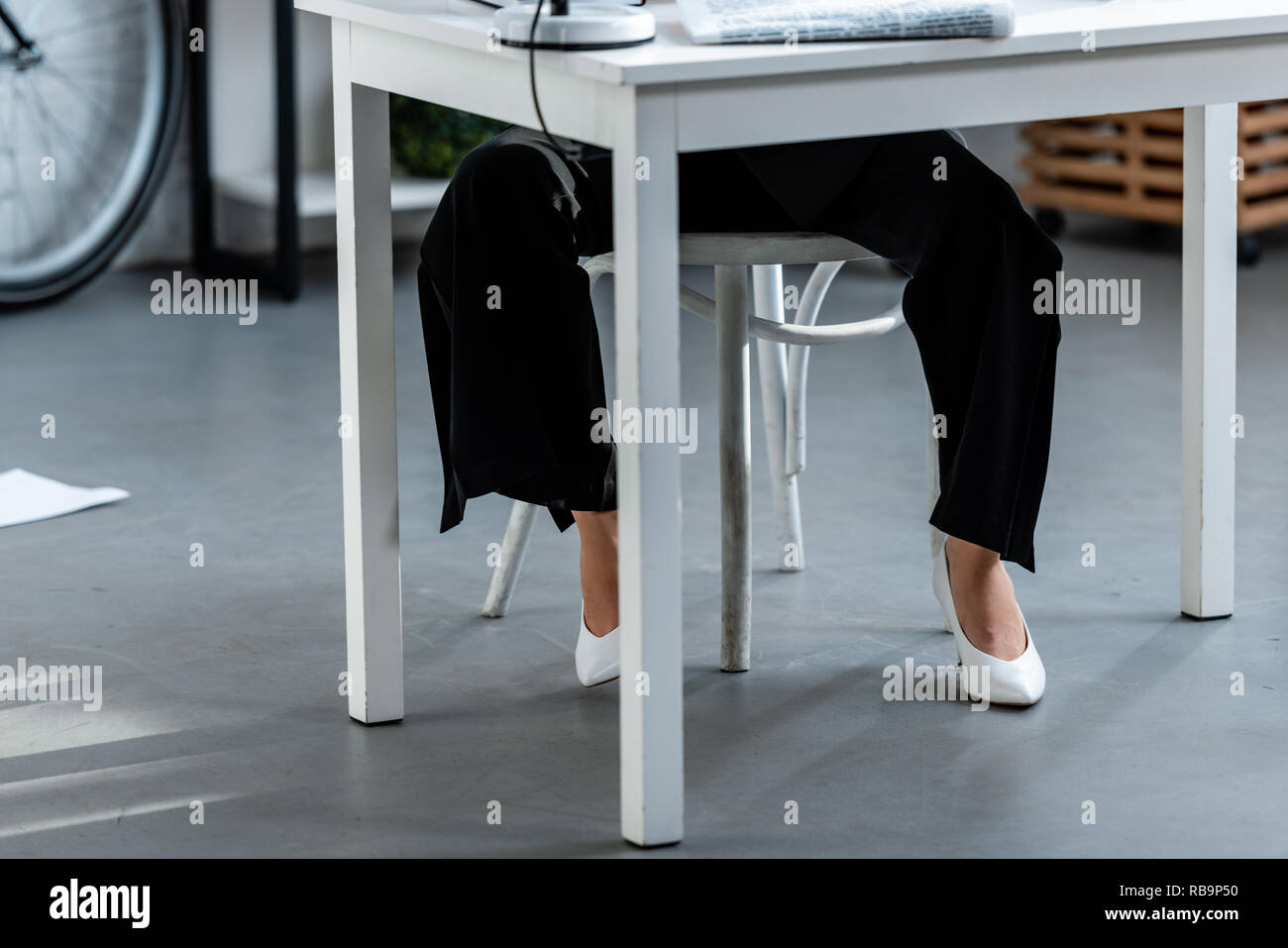 7/8-Ansicht der Frau in Weiß Schuhe und Hose am Tisch sitzen am Arbeitsplatz Stockfoto