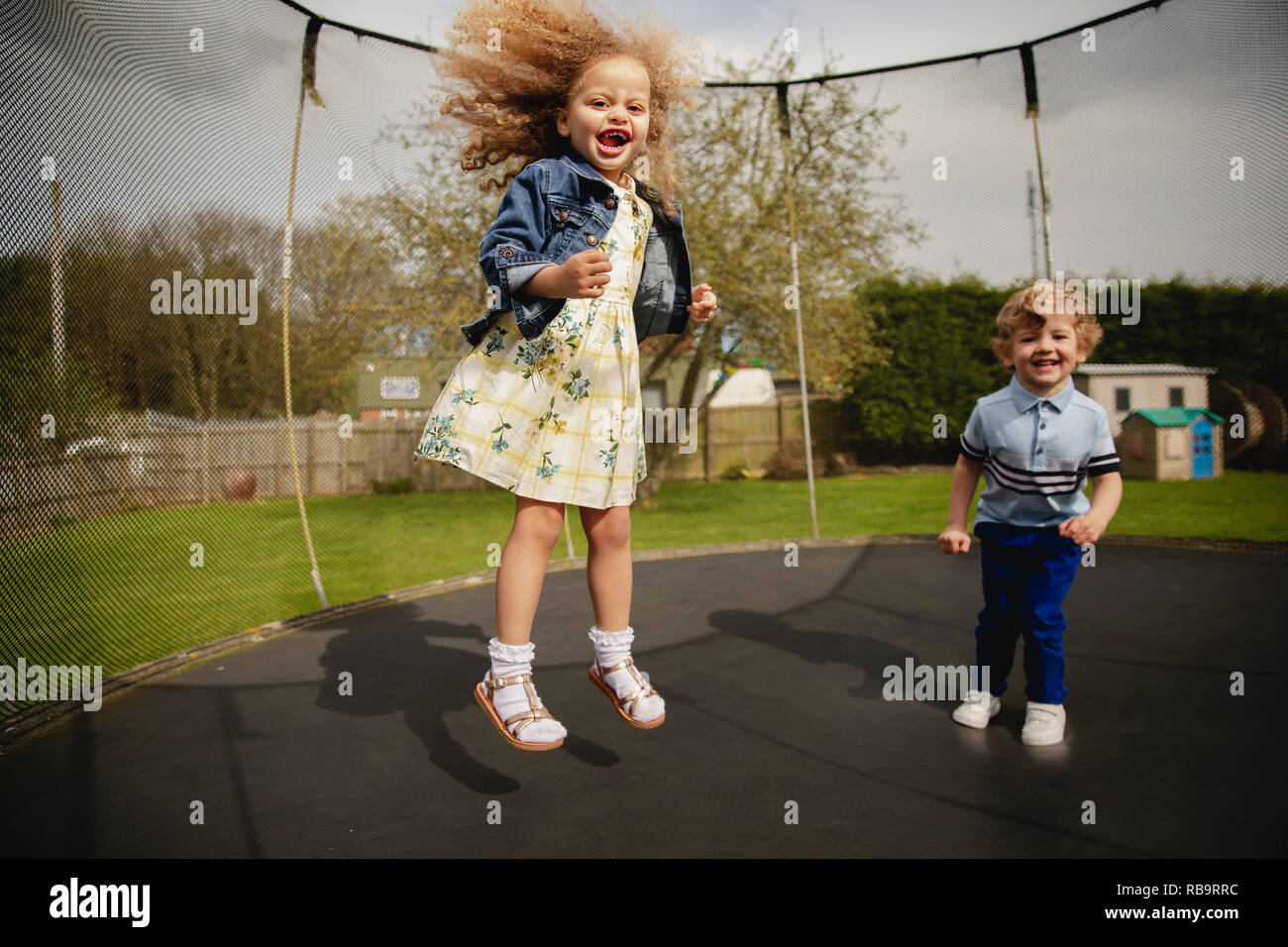 Kleine Mädchen und Jungen spielen auf einem tramploine außerhalb. Sie haben Spaß und verspielt. Stockfoto