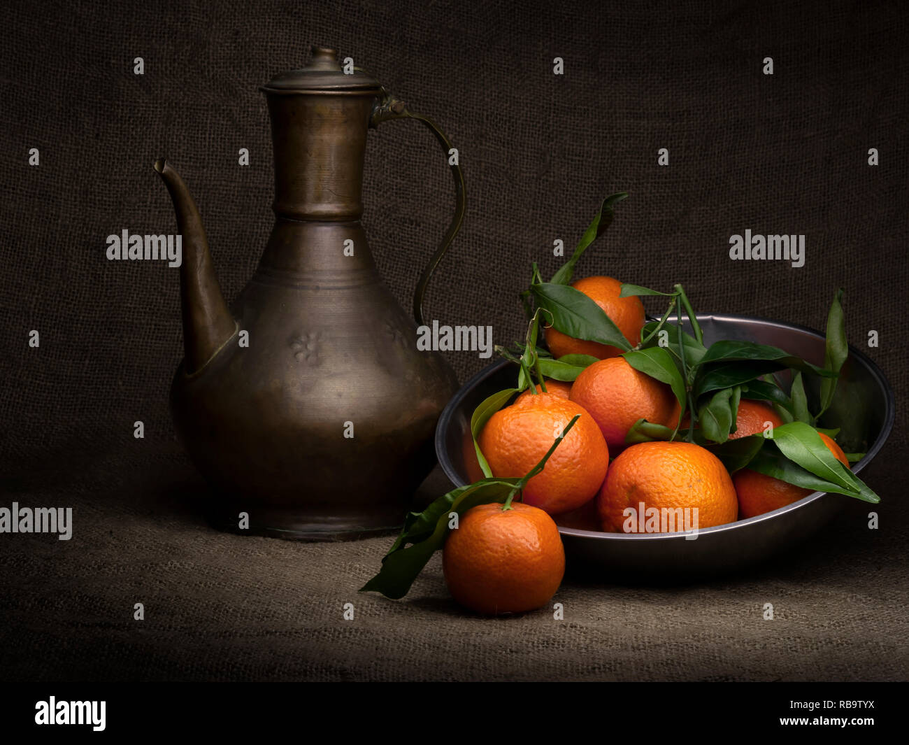 Tee und Orangen. Mehrere Obst in einem Metallbehälter mit alten kupfernen Teekanne. Licht gemalt mit Copyspace und Vignette. Stockfoto