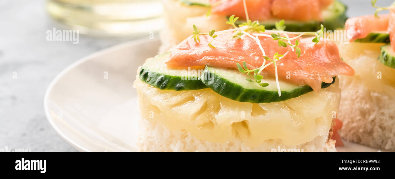 Bruschetta Toast von Weißbrot mit Scheiben Ananas Gurken Fisch Lachs und frisches Grün sprießt. Auf einem weißen Teller am Tisch serviert mit mineralischen w Stockfoto