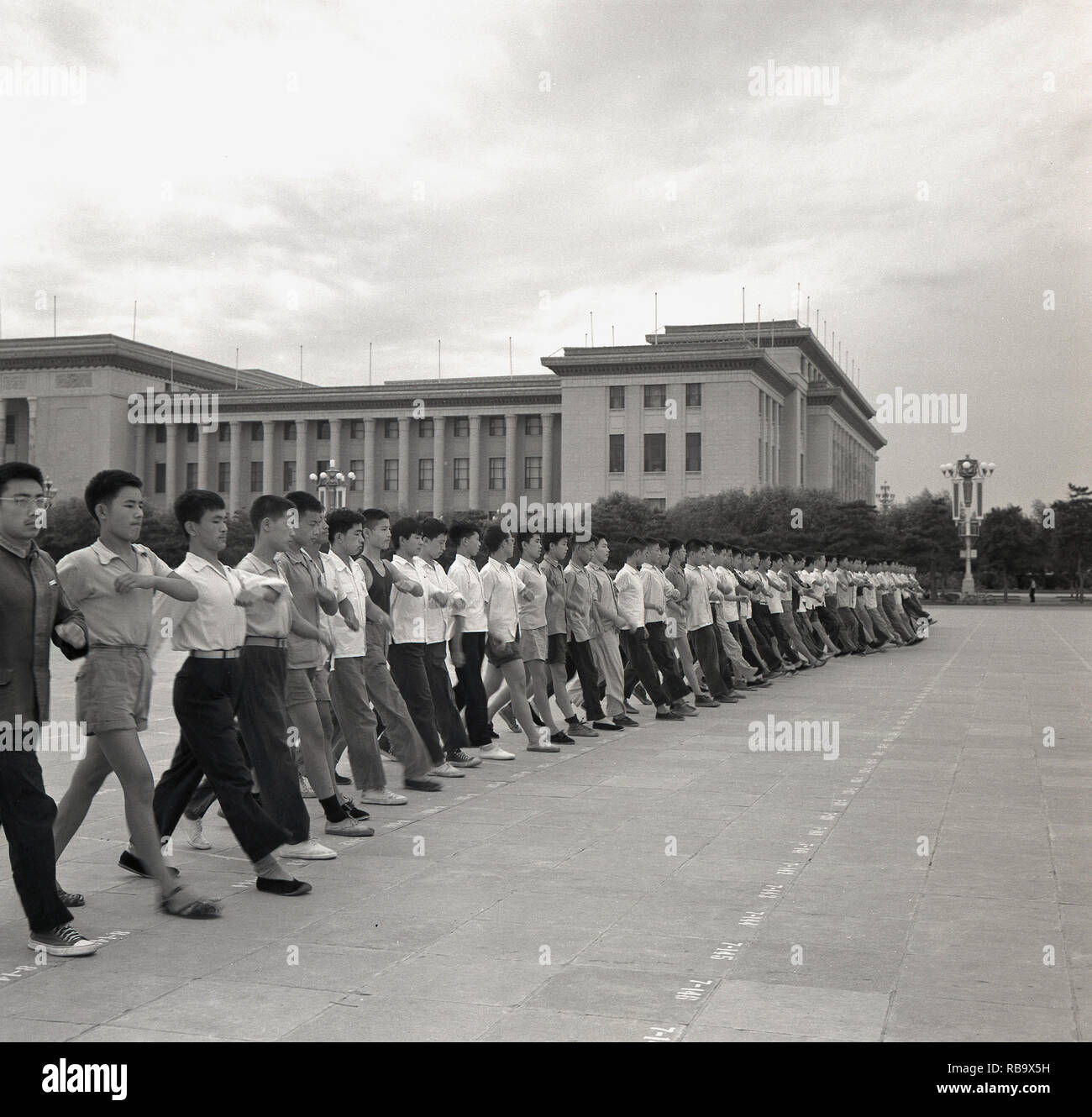 1960, Beijing, China, grosse Gruppe von jungen chinesischen Männer mit zivilen, militärischen Typ clothiing marhcing Übungen auf dem Platz des Himmlischen Friedens ausserhalb des "Großen Halle des Volkes', die People's National Congress Gebäude, dem chinesischen Parlament. Die Vorbereitungen für "Nationalen Tag', die feiert das Ende des chinesischen Bürgerkrieges und der Gründung der People's Repubic unter dem Vorsitzenden Mao Zedong. Stockfoto