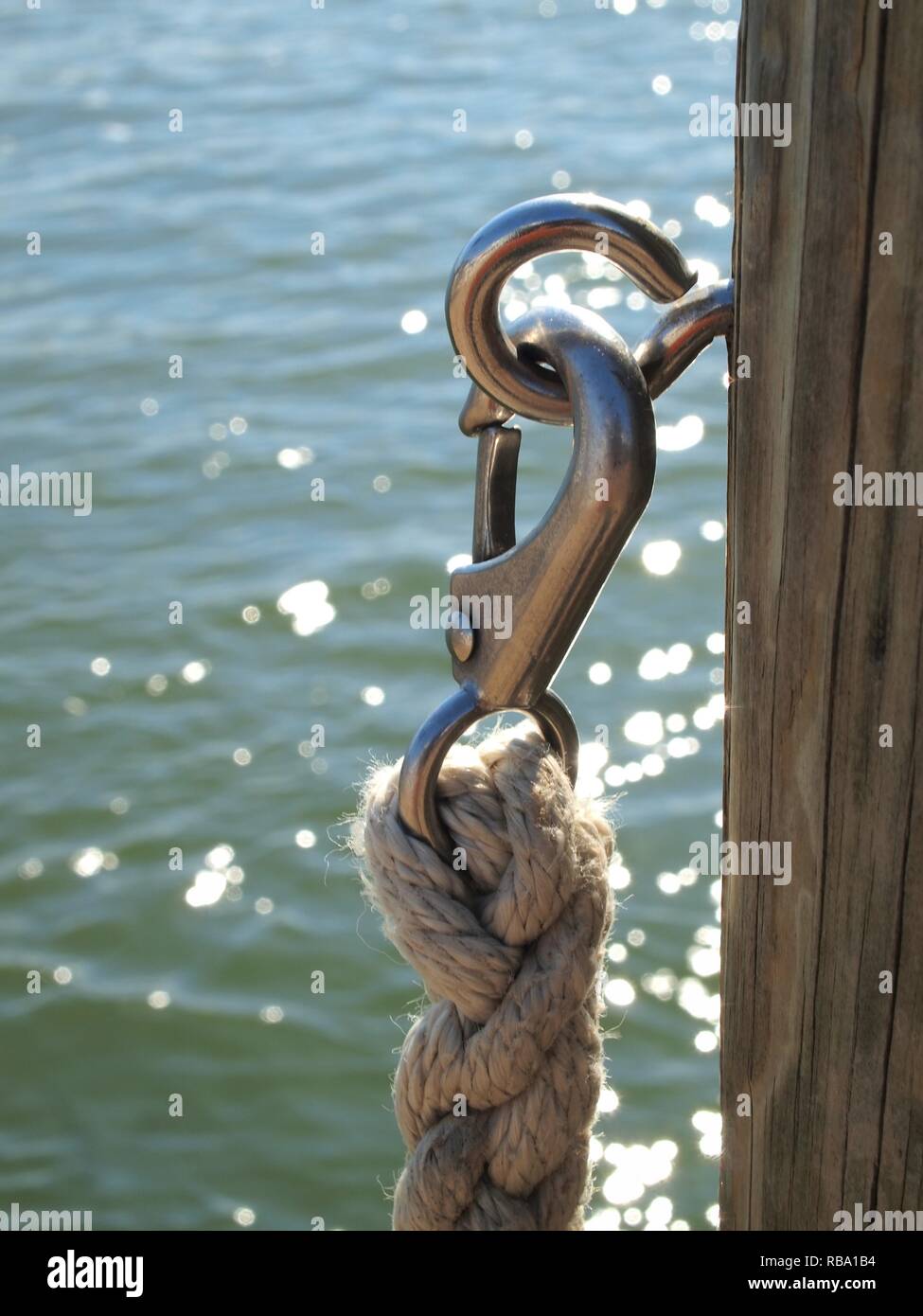 Geflochtenes nautisches Seil und Metallclip auf hölzerner Dock Post. Vertikales Bild mit Minimalismus, Farbe und Texturen. Blick vom Dock auf Kent Island i Maryland Stockfoto