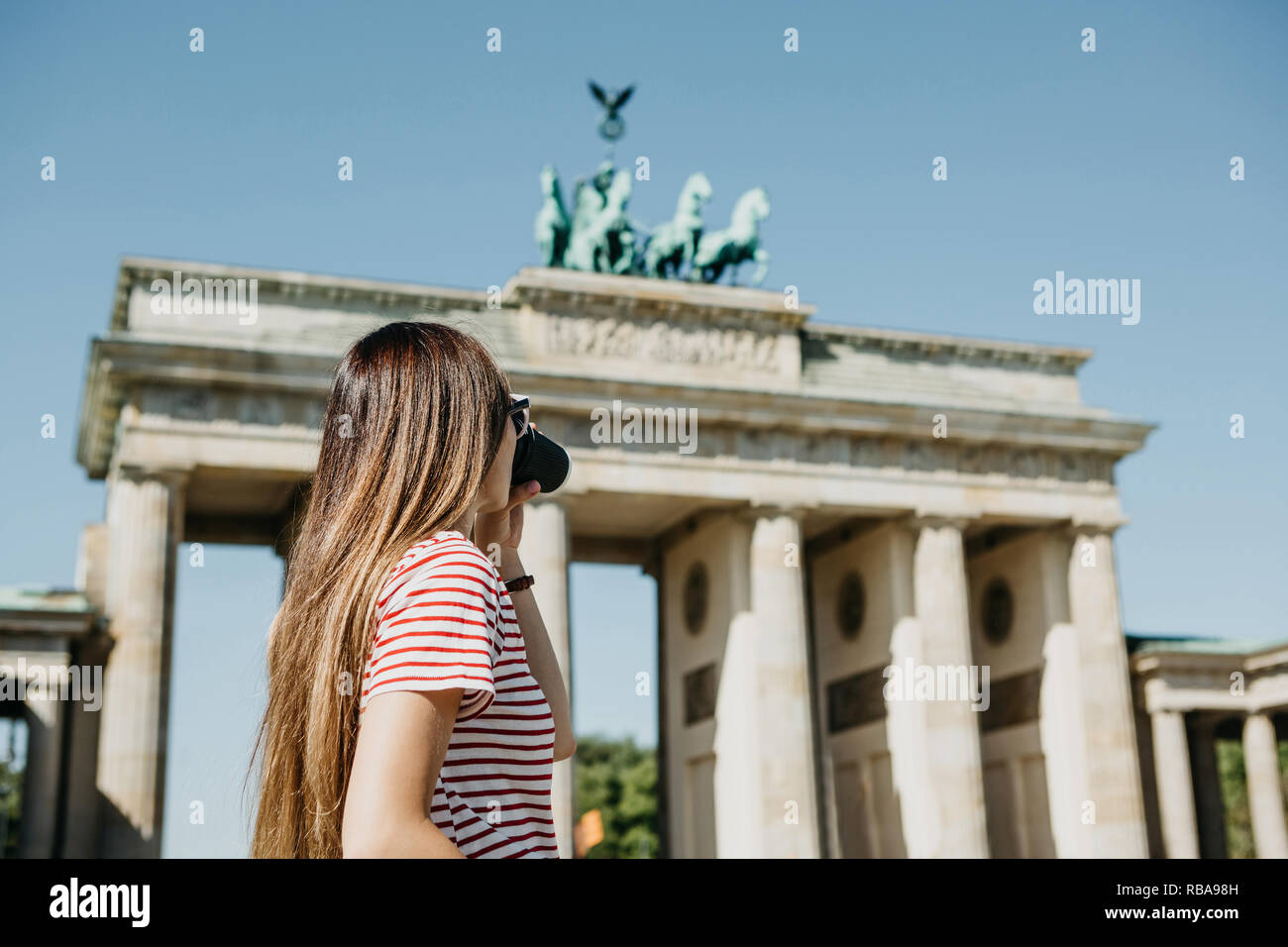 Eine Person, die Getränke aus einer Tasse Kaffee oder einem anderen Getränk bei einem Spaziergang oder beim Sightseeing in Berlin in Deutschland. Die Zukunft ist das Brandenburger Tor. Stockfoto