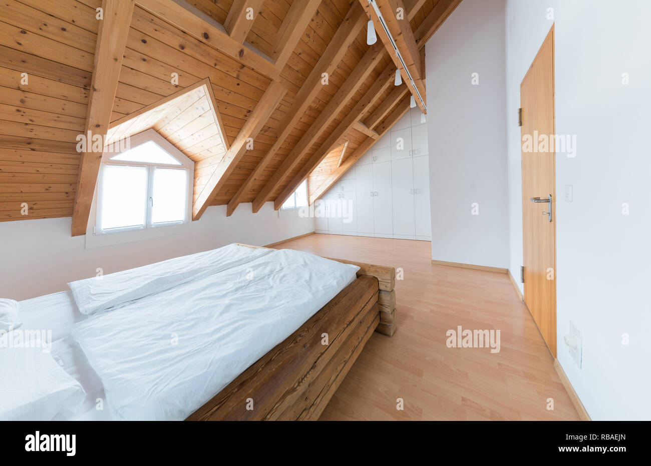 Helles Licht einfache moderne Schlafzimmer mit Parkett und Designer Schrank und traditionellen Holzbalken Bett unter der Dachschräge in einem re Stockfoto