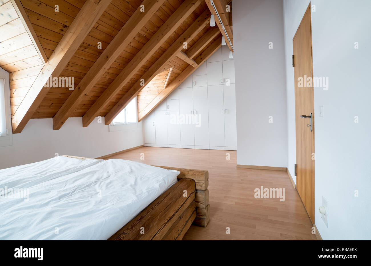 Helles Licht einfache moderne Schlafzimmer mit Parkett und Designer Schrank und traditionellen Holzbalken Bett unter der Dachschräge in einem re Stockfoto