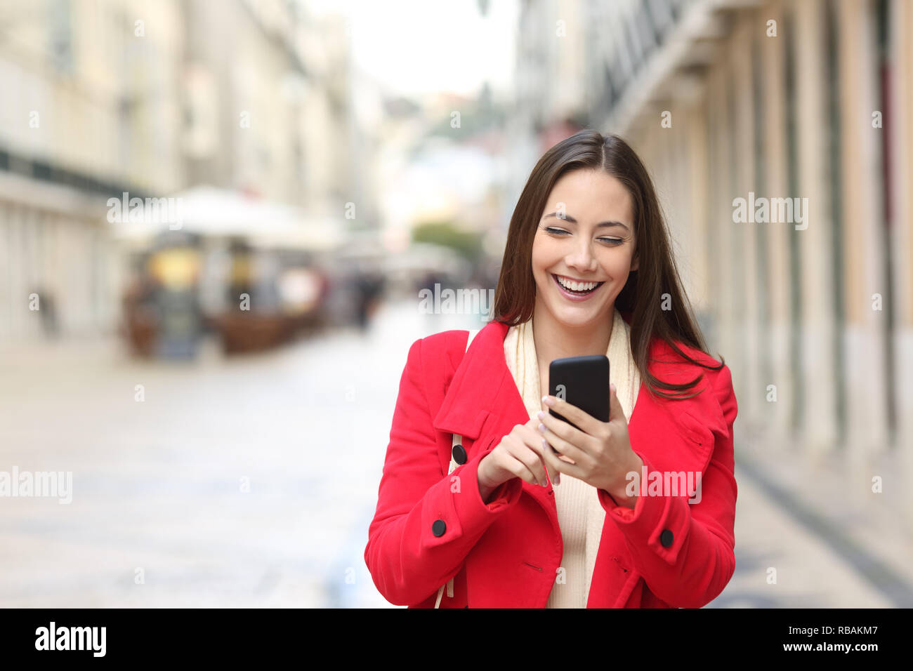 Vorderansicht eines glücklichen Frau in Rot Walking mit Smart Phone auf der Straße im Winter Stockfoto