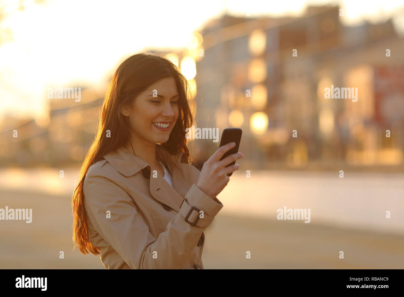 Glückliche Frau mit einem smart phone Spaziergang bei Sonnenuntergang auf der Straße Stockfoto