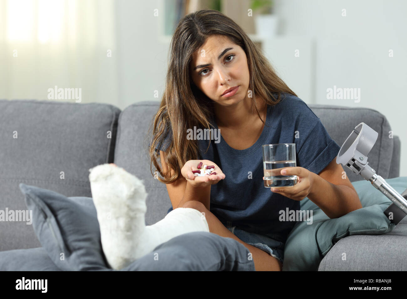 Traurig behinderte Frau mit Pillen an der Kamera sitzt auf einer Couch im Wohnzimmer zu Hause Stockfoto