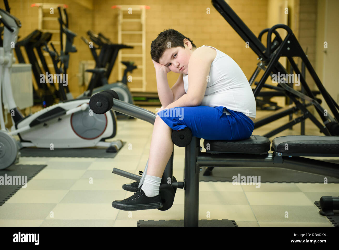 Traurig nachdenklich Fett kleiner Junge sitzt auf Fitnessgeräte im Innenbereich gym Übergewicht Problem lösen. Stockfoto