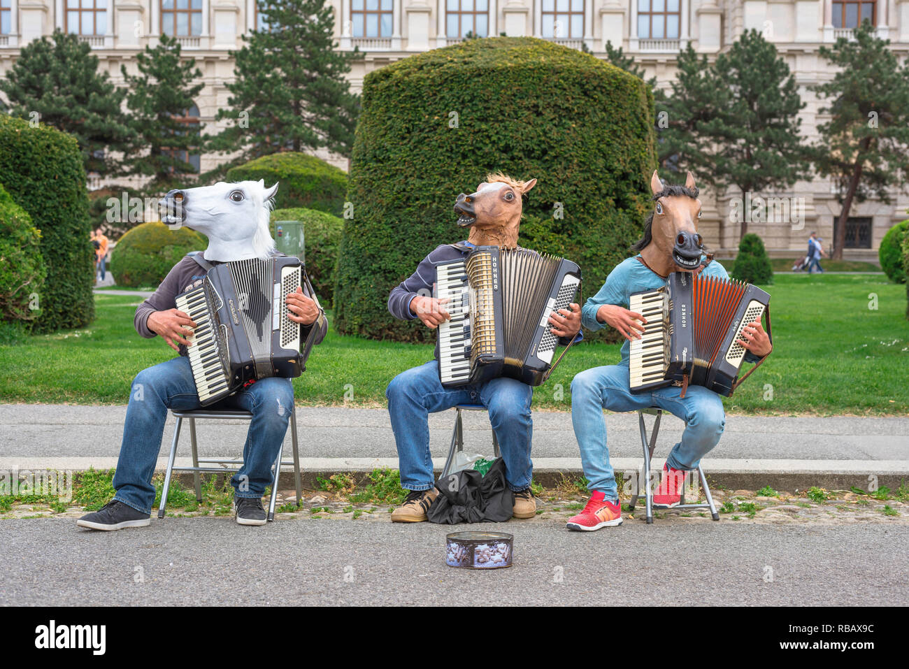 Buskers Straßentheater, ein Trio von akkordeonisten tragen bizarre Kopfbedeckungen spielen für Passanten in Maria Theresienplatz, Wien, Wien, Österreich. Stockfoto