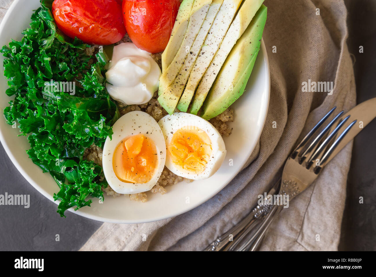 Quinoa buddha Schüssel mit gebackenen Tomaten, Avocado, Grünkohl, gekochte Eier und griechischer Joghurt auf grauem Beton Hintergrund. Gesundes Frühstück. Ansicht von oben. Stockfoto