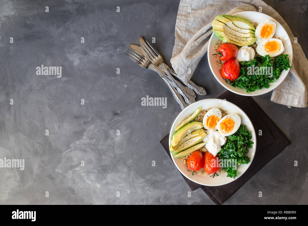 Quinoa buddha Schüsseln mit gebackenen Tomaten, Avocado, Grünkohl, gekochte Eier und griechischer Joghurt auf grauem Beton Hintergrund. Gesundes Frühstück. Ansicht von oben. Kopieren Sie sp Stockfoto