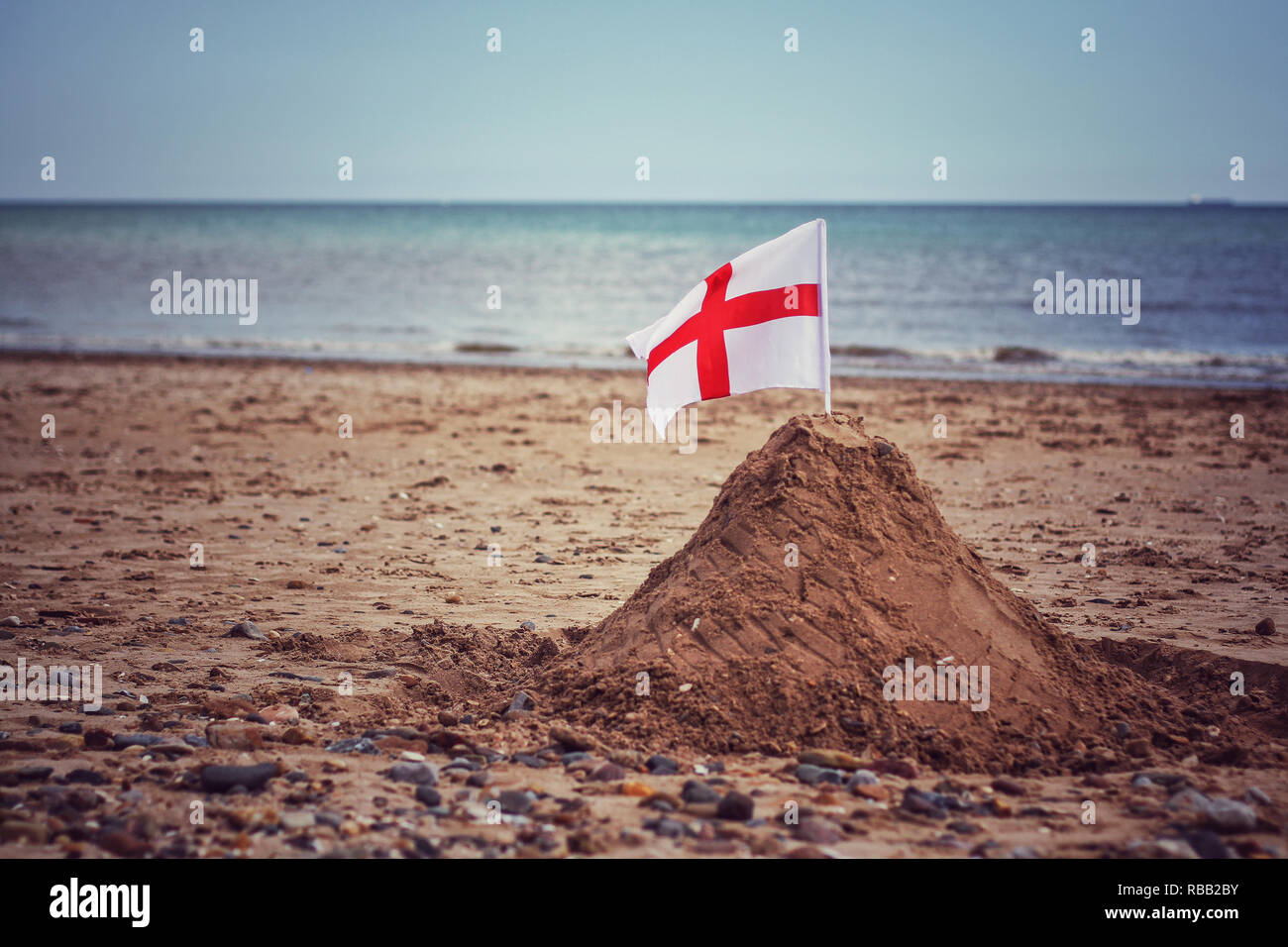 Ein englischer St. George's Cross Flag in einem Sandcastle auf einem Britischen Strand, die Grenze und Boundary Control Während der illegalen Einwanderung in Großbritannien Stockfoto