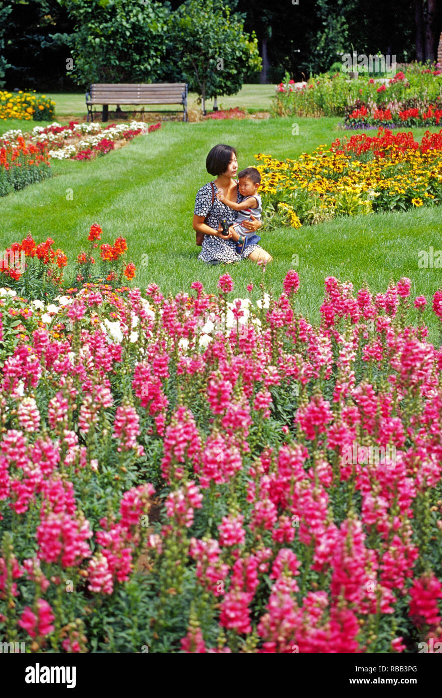 Eine asiatische Frau hält Ihr kleines Kind beim Sitzen inmitten einer Wiese mit Blumen in einem Park in Rapid City, South Dakota Stockfoto