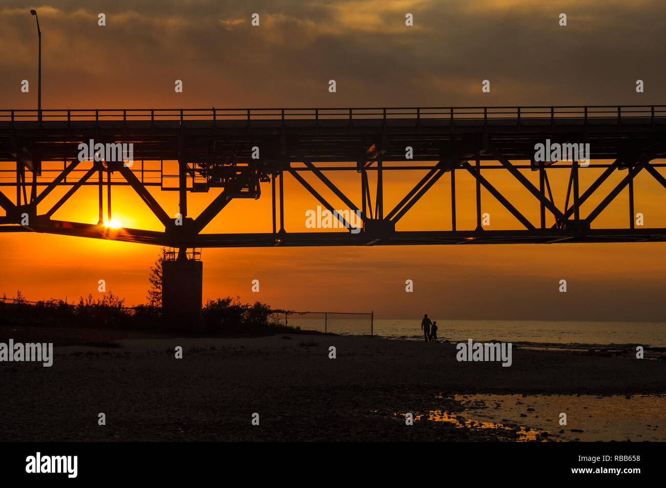 Vater und Sohn Silhouette zu Fuß am Strand unter Mackinaw Bridge bei Sonnenuntergang Stockfoto