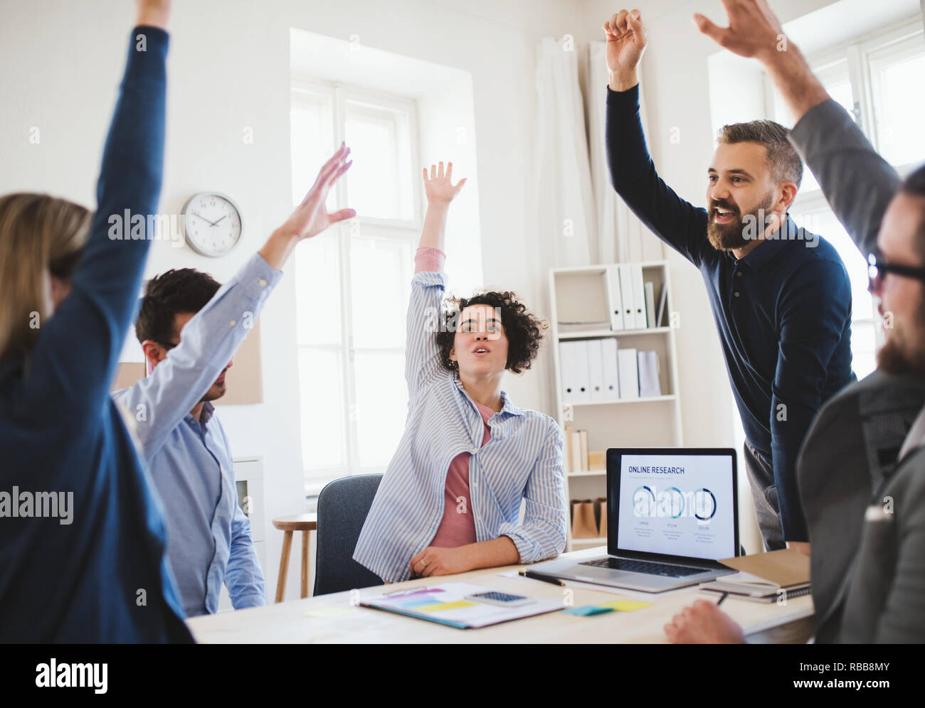 Junge Geschäftsleute sitzen um den Tisch in einem modernen Büro, Erfolg feiern. Stockfoto