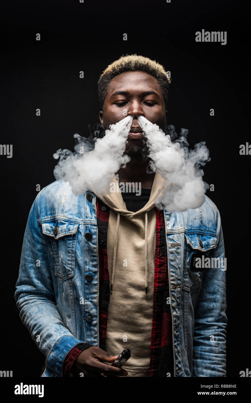 Junge afrikanische Mann Rauch vape auf dunklem Hintergrund isoliert Stockfoto