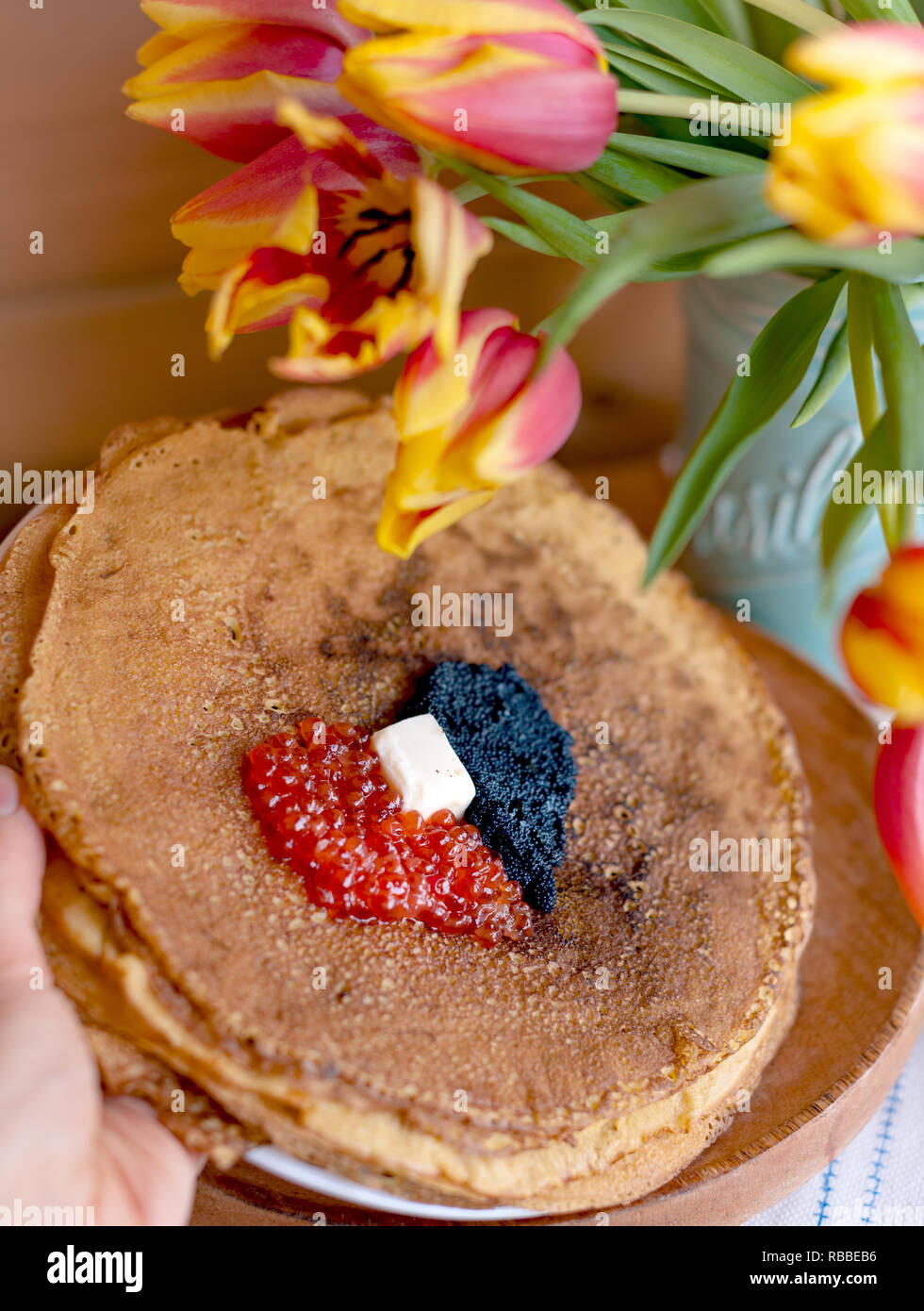 Pfannkuchen für die traditionellen russischen Frühling Urlaub. Dünne Pfannkuchen mit roter und schwarzer Kaviar und einen Strauß mit frischen Tulpen. Holz- Hintergrund und fest Stockfoto
