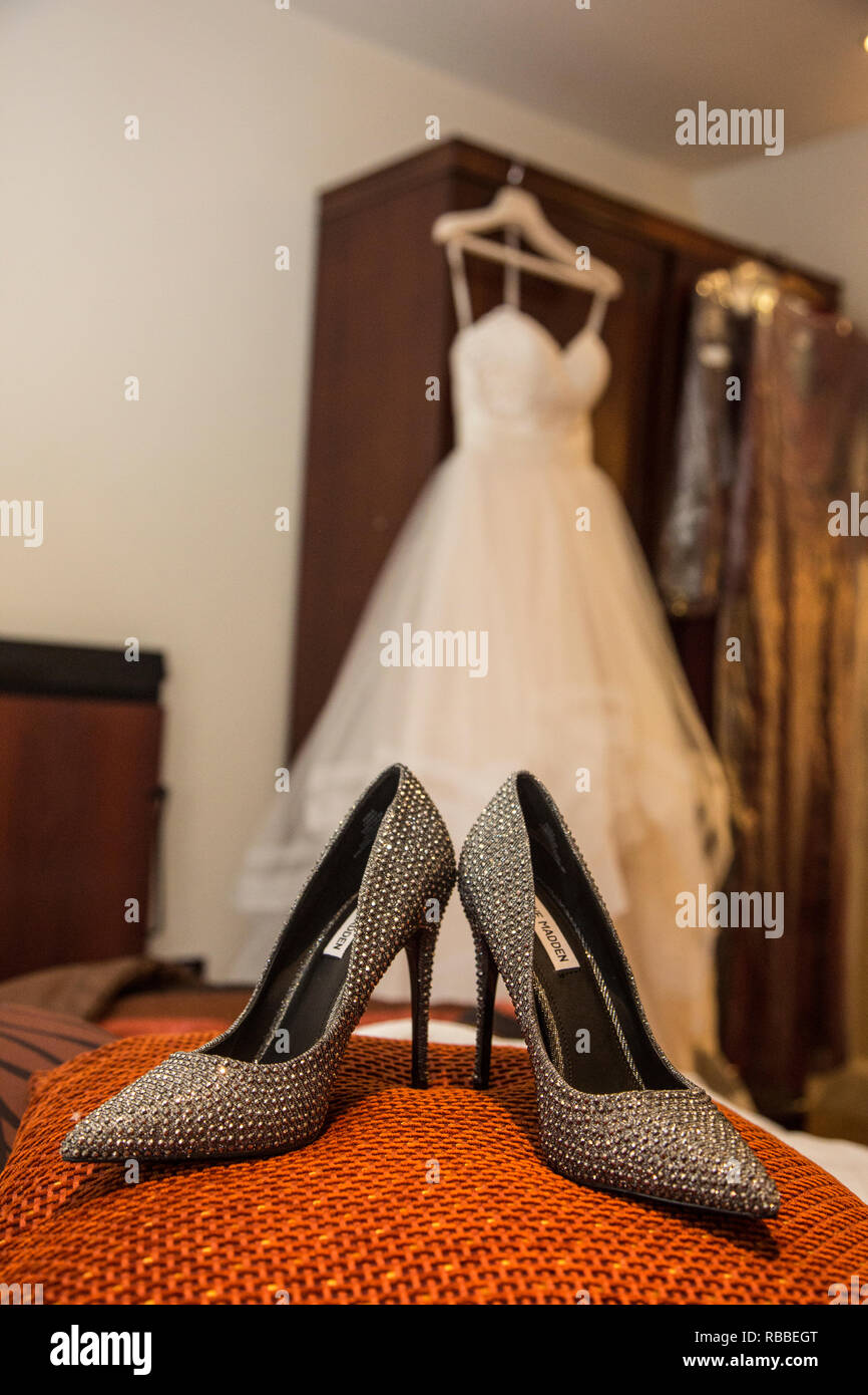 Sparkly Bräute Schuhe auf einem orangefarbenen Kissen mit der Bräute dress up Hängen im Hintergrund wartet an Ihrem Hochzeitstag getragen zu werden. Stockfoto