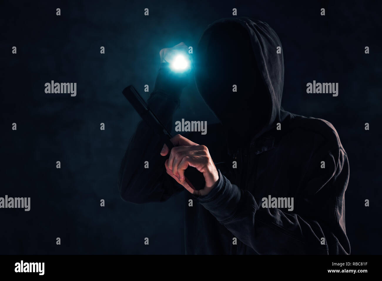 Bewaffneter Raub, Kriminelle mit Hoodie holding Gun und Fackelschein und angreifenden in dunklen, Low Key selektiven Fokus Stockfoto