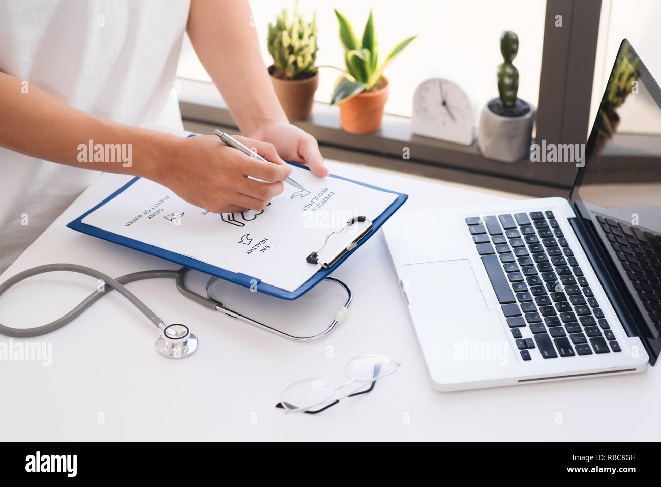 Nahaufnahme auf die Hände. Asiatische Frau Doktor mit Laptop und schreiben etwas auf die Zwischenablage, Rezept, Schreibarbeit, Patienten Checkliste Papier oder Anwendung Stockfoto