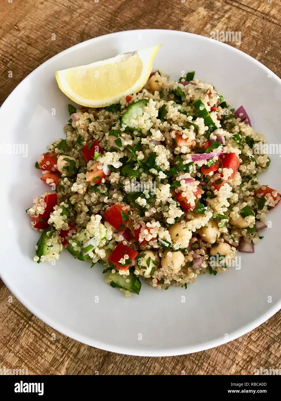 Eine gesunde und farbenfrohe vegan Quinoa Salat mit Zitrone Keil auf einem Holztisch Stockfoto