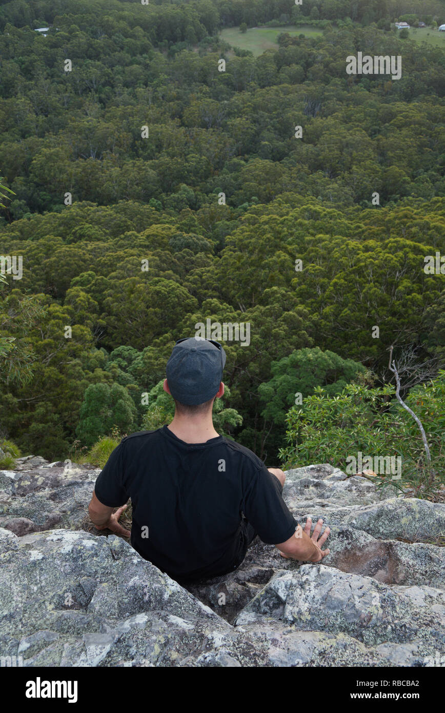 Mann sitzt auf der Kante einer Klippe auf einem Wald Stockfoto