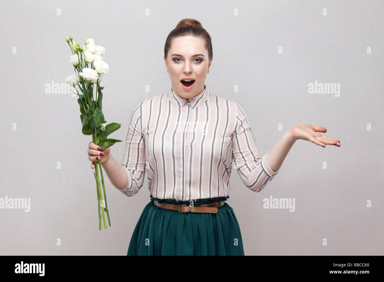 Unglaublich. Portrait von romantische junge Frau im gestreiften Hemd und grün Rock holding Blumenstrauß aus den weißen Blüten mit erhobenen Armen überrascht. Hallenbad, st Stockfoto