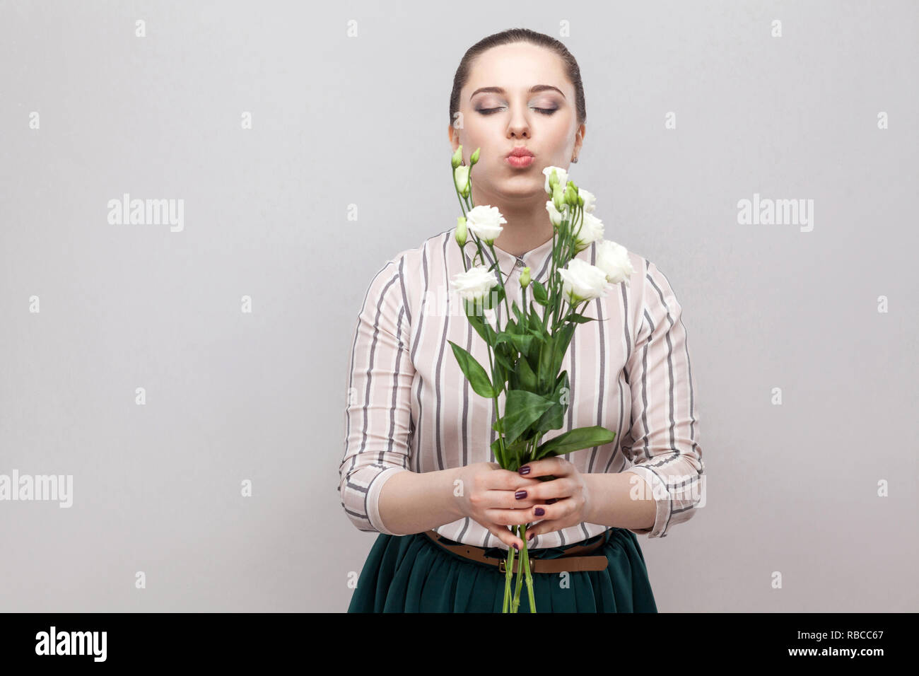 Portrait von attraktiven Romantische schöne junge Frau im gestreiften Hemd und grün Rock holding Blumenstrauß aus den weißen Blüten und Senden von Luft küssen. Hallenbad, Stu Stockfoto