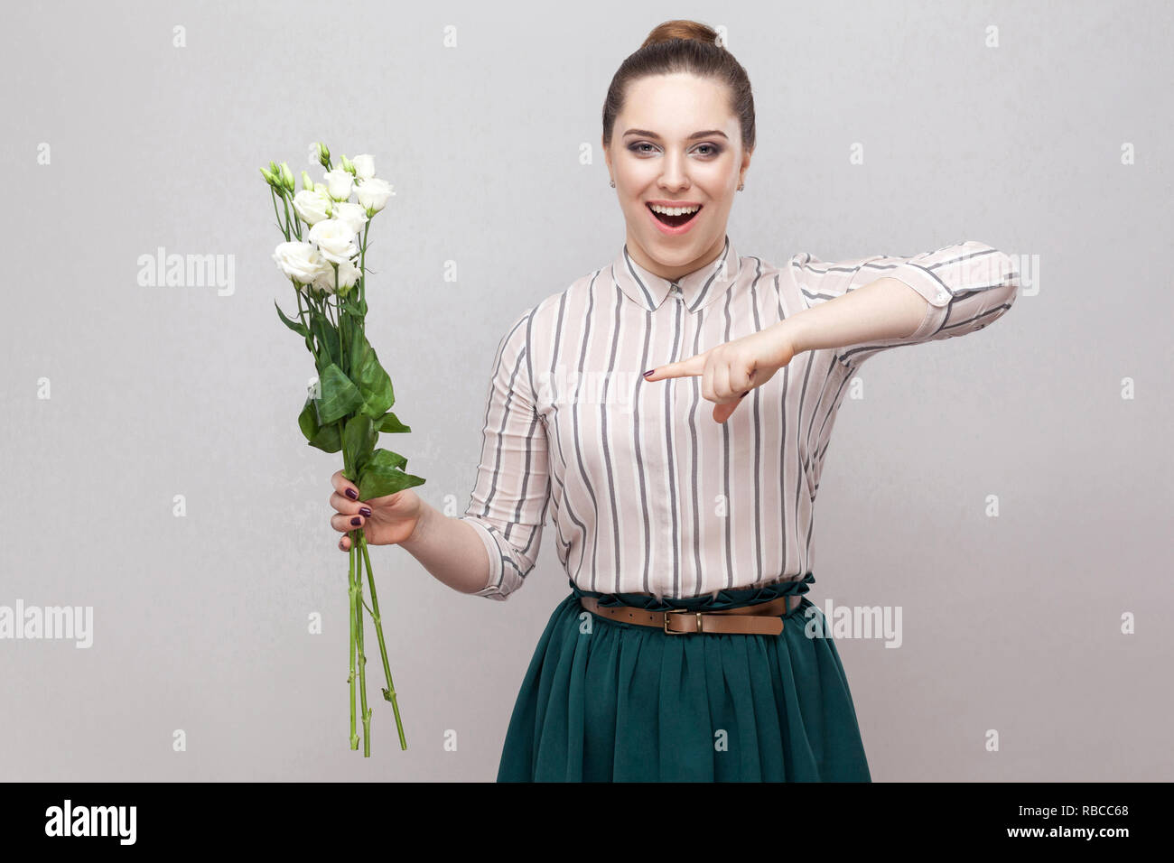 Portrait von überrascht attraktive romantische junge Frau im gestreiften Hemd und grün Rock holding Blumenstrauß aus den weißen Blüten und Zeigefinger. Hallenbad, st Stockfoto