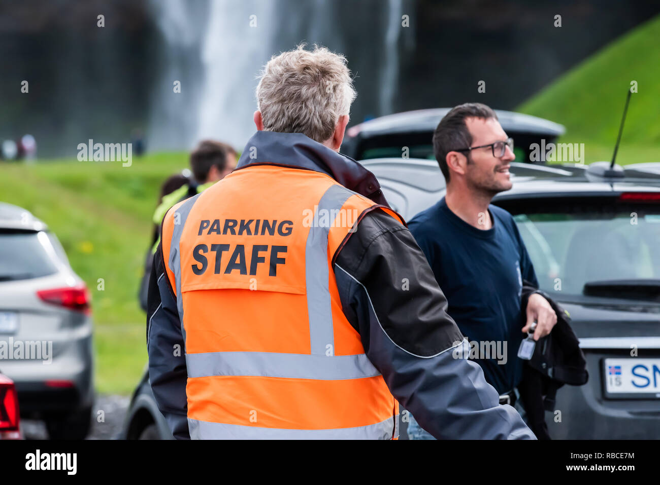 Seljalandsfoss, Island - 14. Juni 2018: Parkplatz mit Wasserfall mit Nahaufnahme des Security Guard officer schreiben Tickets in orange Weste und Touristen w Stockfoto