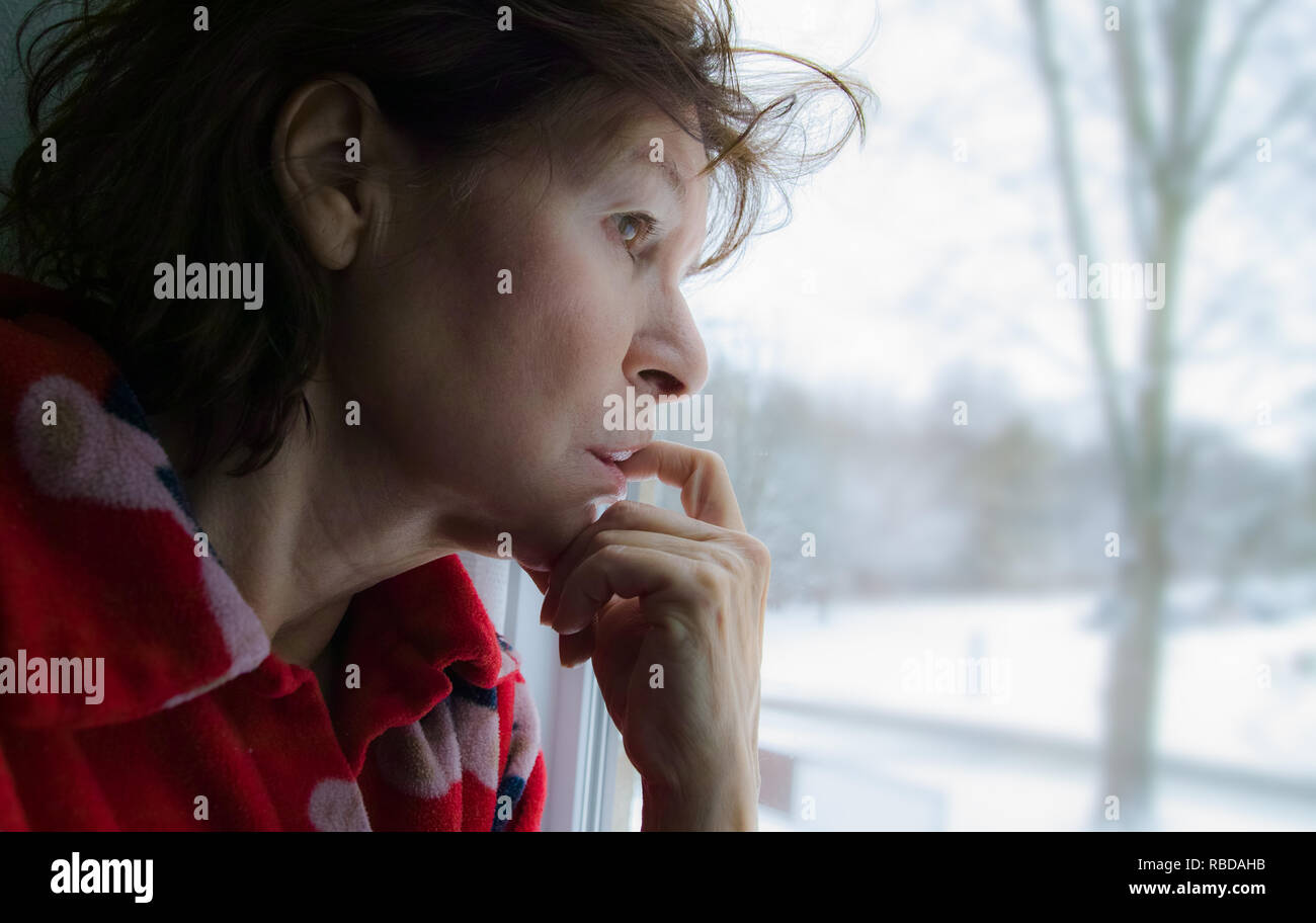 Eine reife Frau beißt seine Nägel während des Wartens und schaut aus dem Fenster. Profil ansehen. Stockfoto