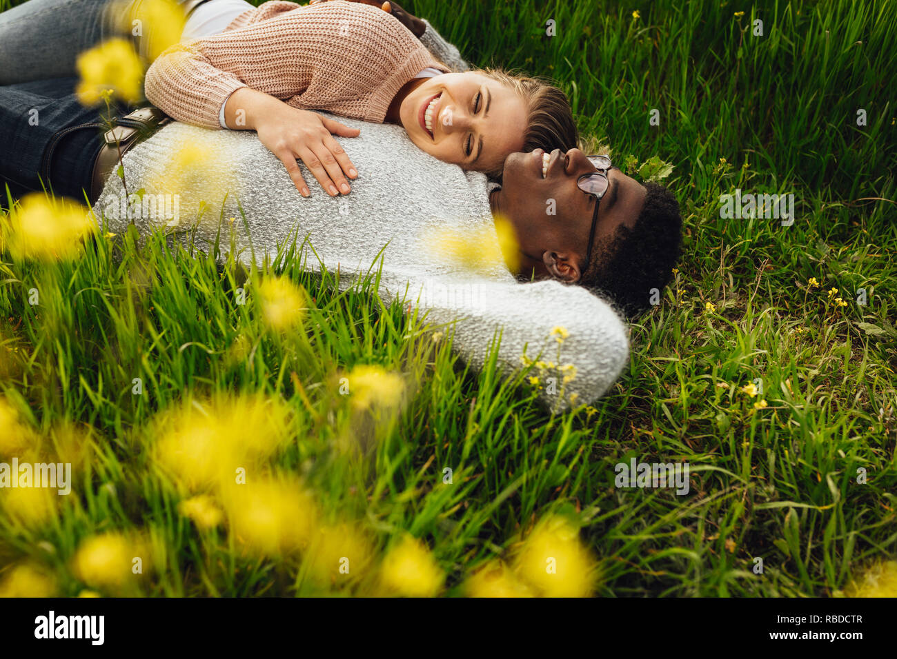 Schöne junge Paar liegen im grünen Gras im Freien. Junger Mann und Frau liegen in der blühenden Wiese im Freien. Stockfoto
