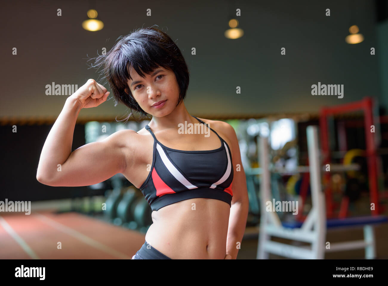 Junge schöne asiatische Frau bicep biegen an der Turnhalle Stockfoto