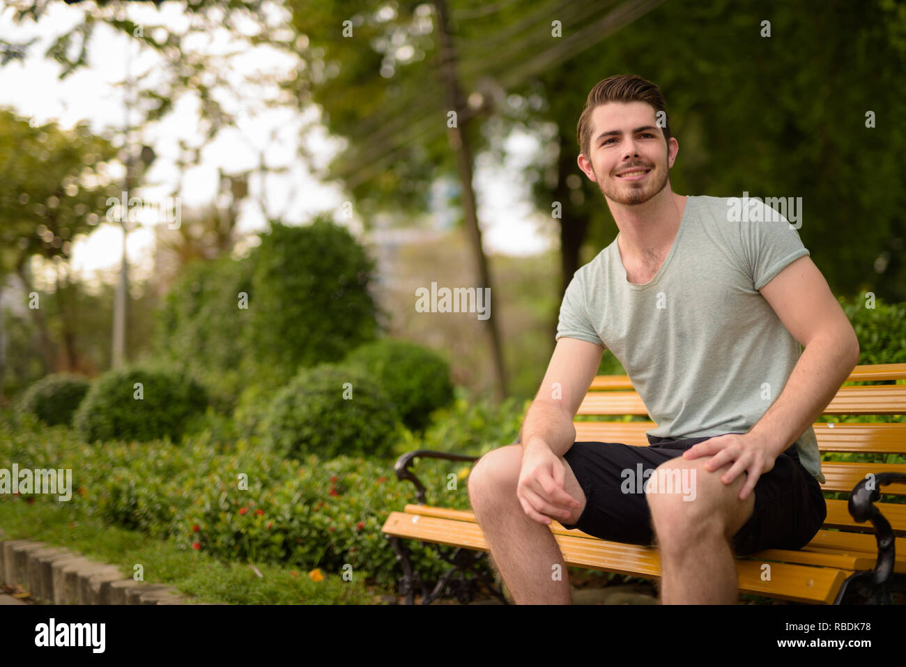 Porträt der jungen gutaussehenden Mann sitzt im Park beim Lächeln Stockfoto