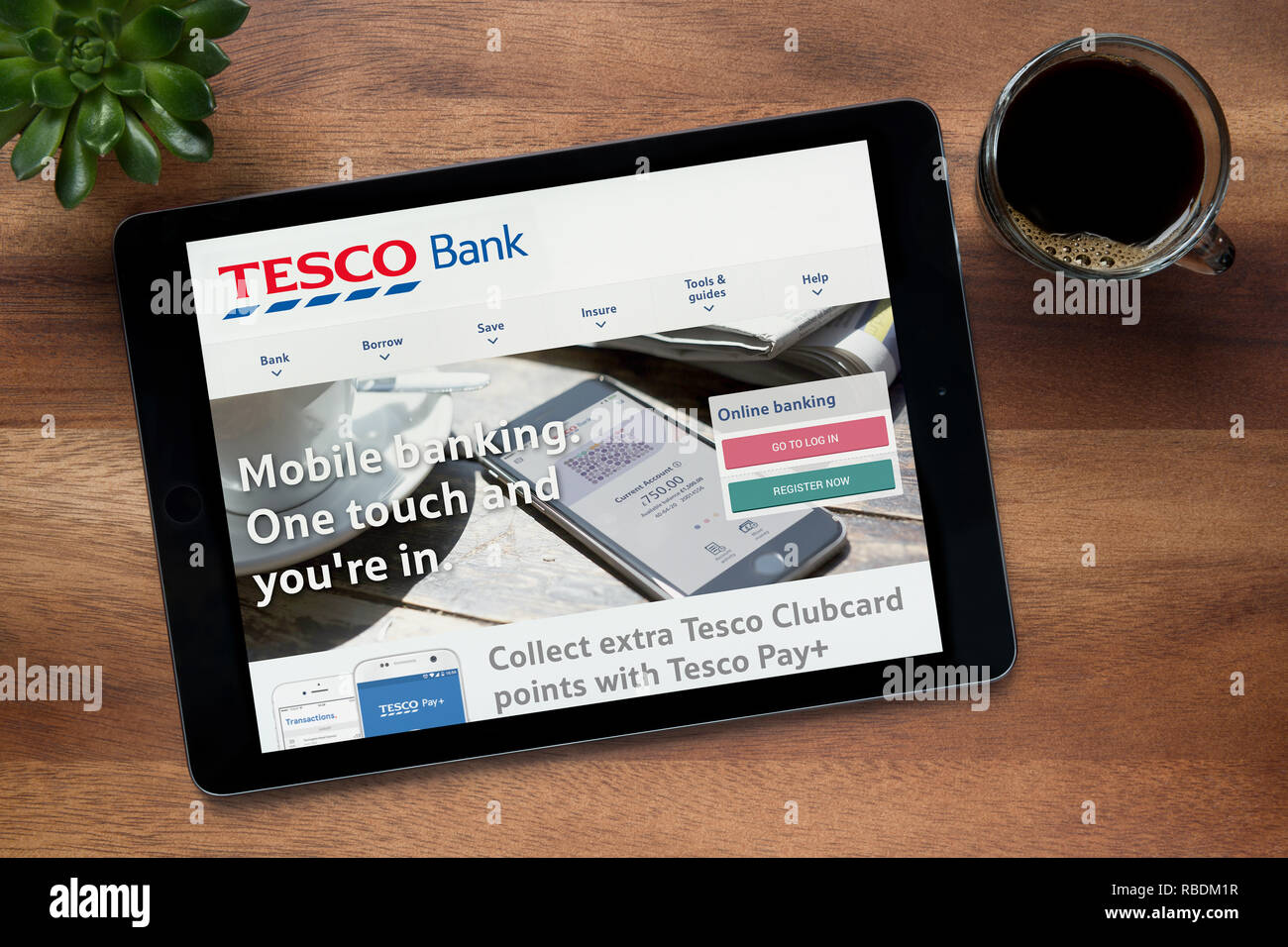 Die Website von Tesco Bank ist auf einem iPad Tablet gesehen, auf einer hölzernen Tisch zusammen mit einem Espresso und einem Haus Anlage (nur redaktionelle Nutzung). Stockfoto