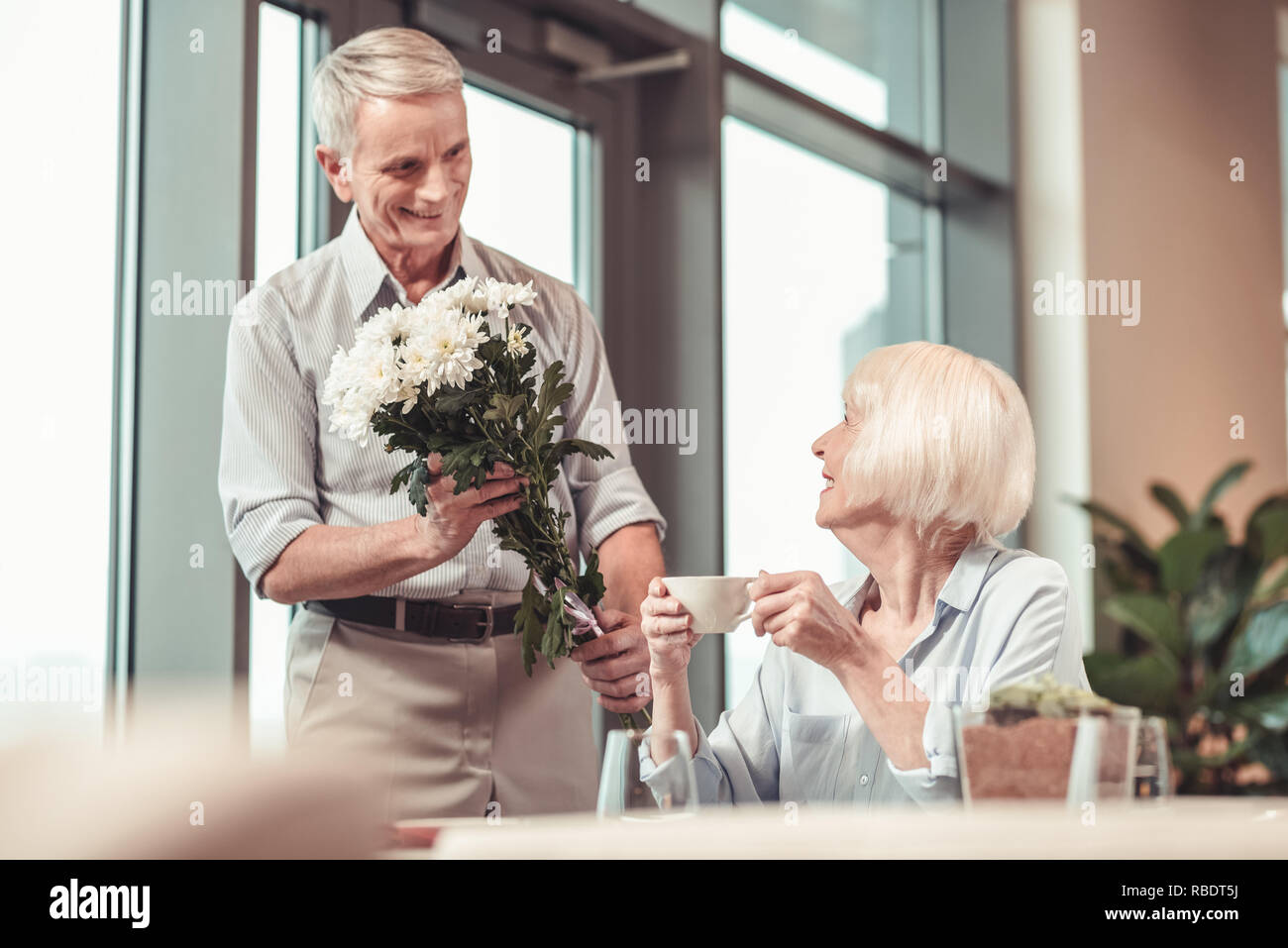 Junge wieder. Glücklich lächelnde Frau mit Blumen von einem Mann in einem Cafe sitzen Stockfoto