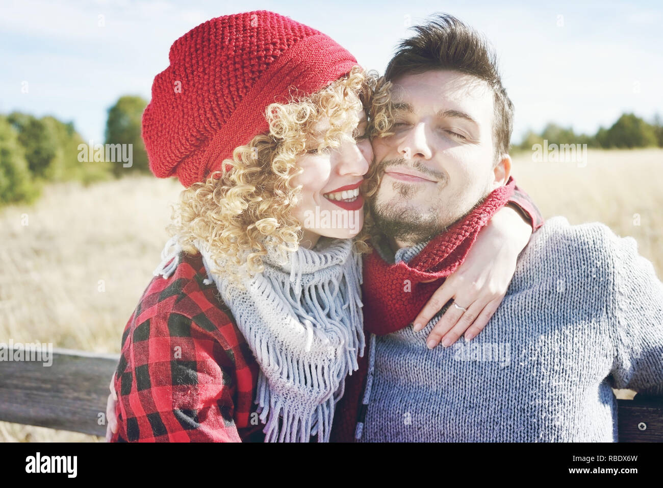 Romantische junge Paar eine schöne blonde Frau mit lockigem Haar und einen roten Wolle gap Umarmungen zu ihrem Freund und ein stattlicher Mann outdoor Stockfoto