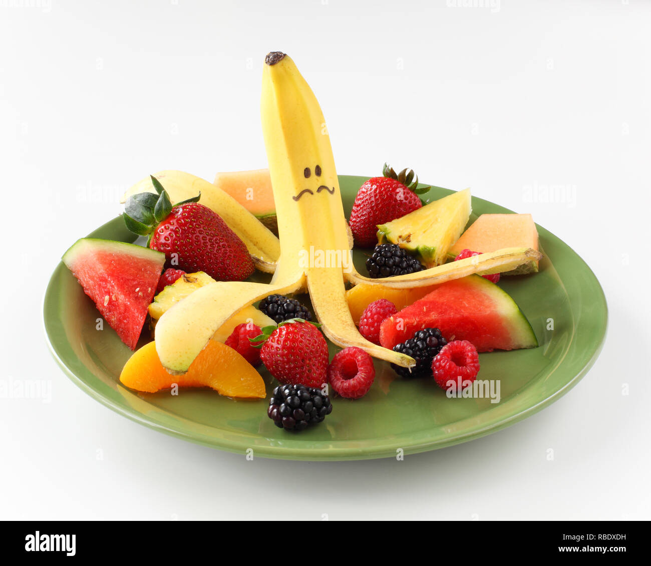 Banane mit lustigen Gesicht auf Platte von Obst wie Beeren und Melonen. Stockfoto