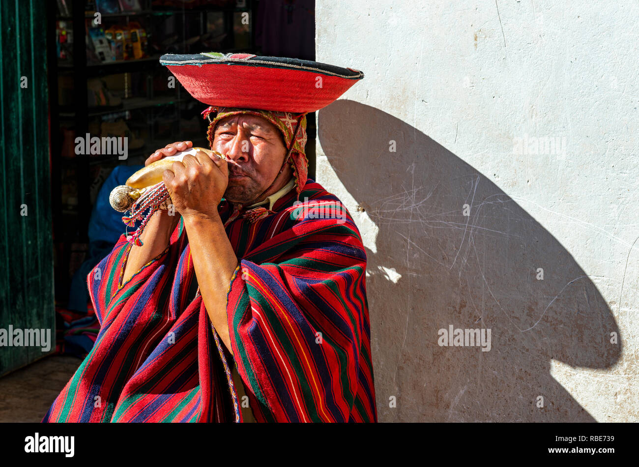 Porträt einer peruanischen Quechua horn Gebläse mit traditioneller Kleidung, Hut und Poncho im Stadtzentrum von Cusco, Peru. Stockfoto