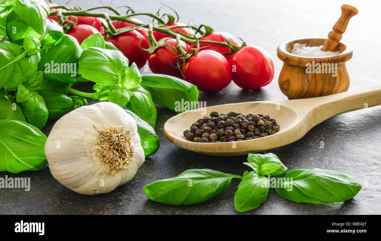 Italienische Küche Zutaten. Kräuter und Gewürze Gewürze. Basilikum, Knoblauch, Tomaten, Salz und Pfeffer auf dunklen Stein. Stockfoto