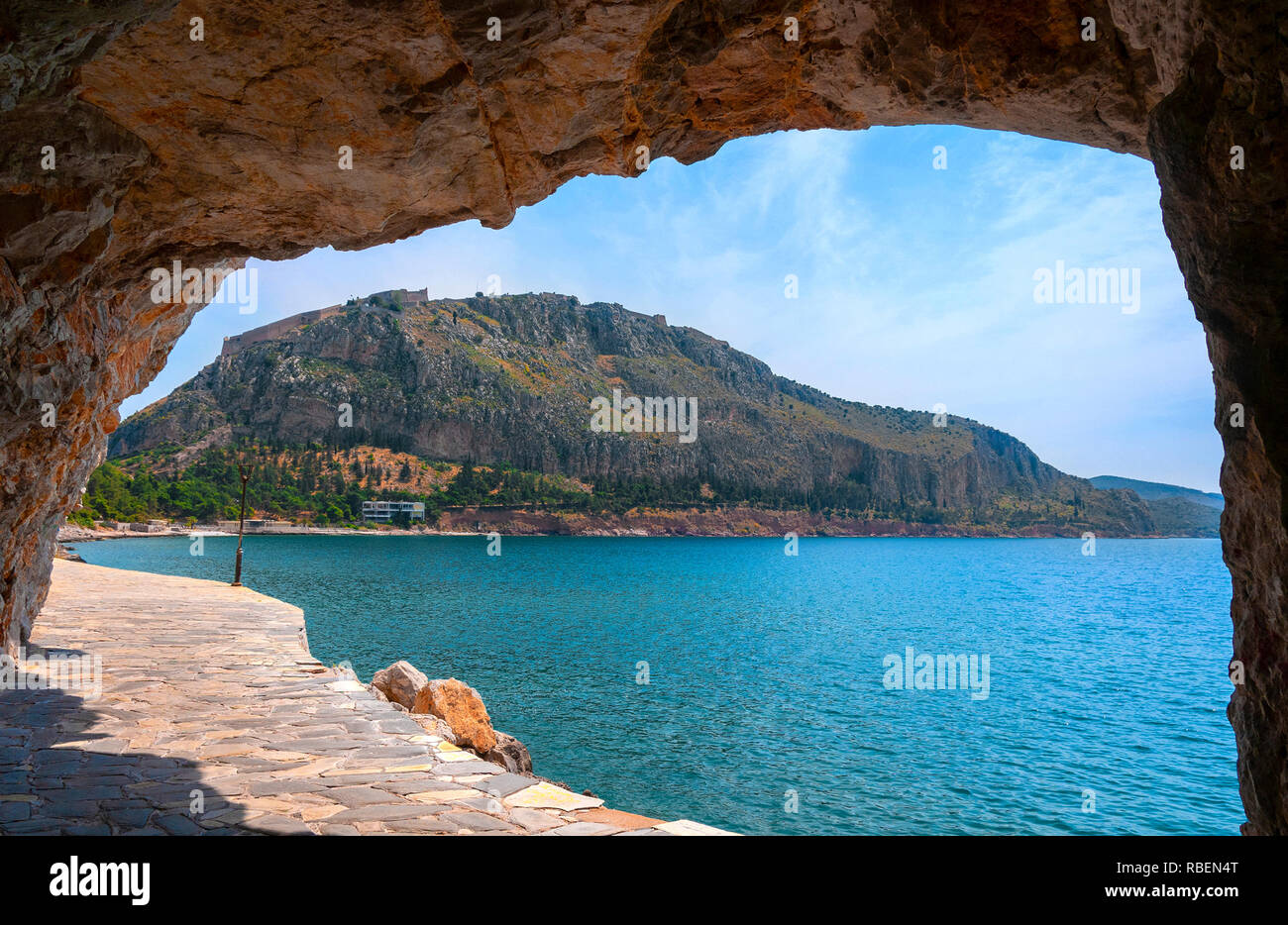 Küstenweg mit großen Felsen Torbogen geben einen Blick auf die Festung Palamidi oder Burg auf dem Acronauplia Halbinsel, Nafplio, Argolis, Peloponnes, Griechenland Stockfoto