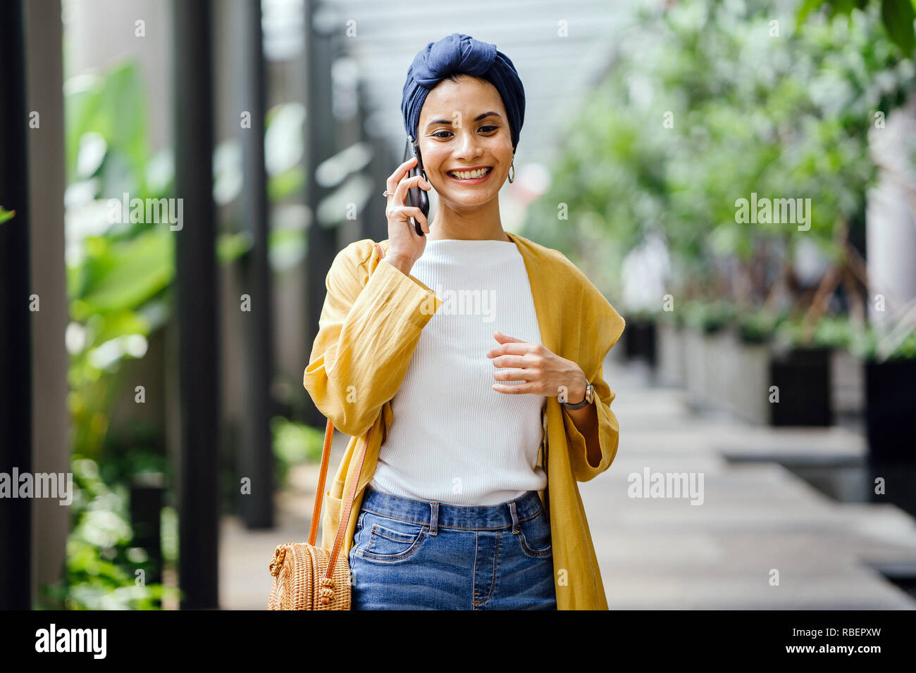 Eine junge und schöne Orientalische Frau in einem turban Hijab ist Lächeln, wie Sie auf Ihrem Smartphone die Gespräche auf der Straße während des Tages. Stockfoto
