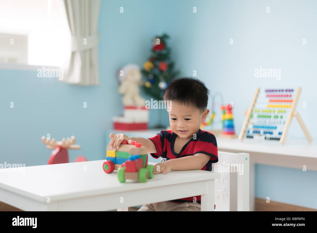 Adorable asiatischen Kleinkind Baby Junge sitzt auf einem Stuhl und Spielen mit Farbe Holz- zug Spielzeug zu Hause. Stockfoto