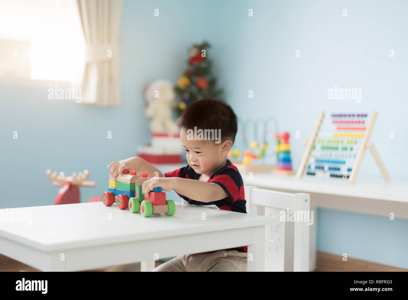 Adorable asiatischen Kleinkind Baby Junge sitzt auf einem Stuhl und Spielen mit Farbe Holz- zug Spielzeug zu Hause. Stockfoto