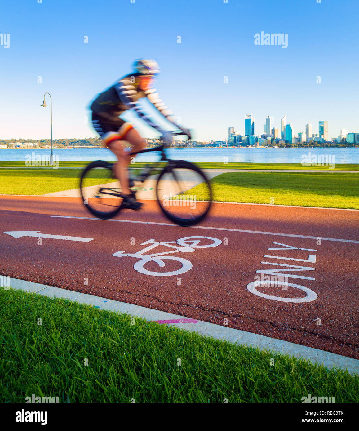 Eine männliche Radsportler, die auf einem Radweg mit der Skyline einer Stadt in der Ferne Stockfoto