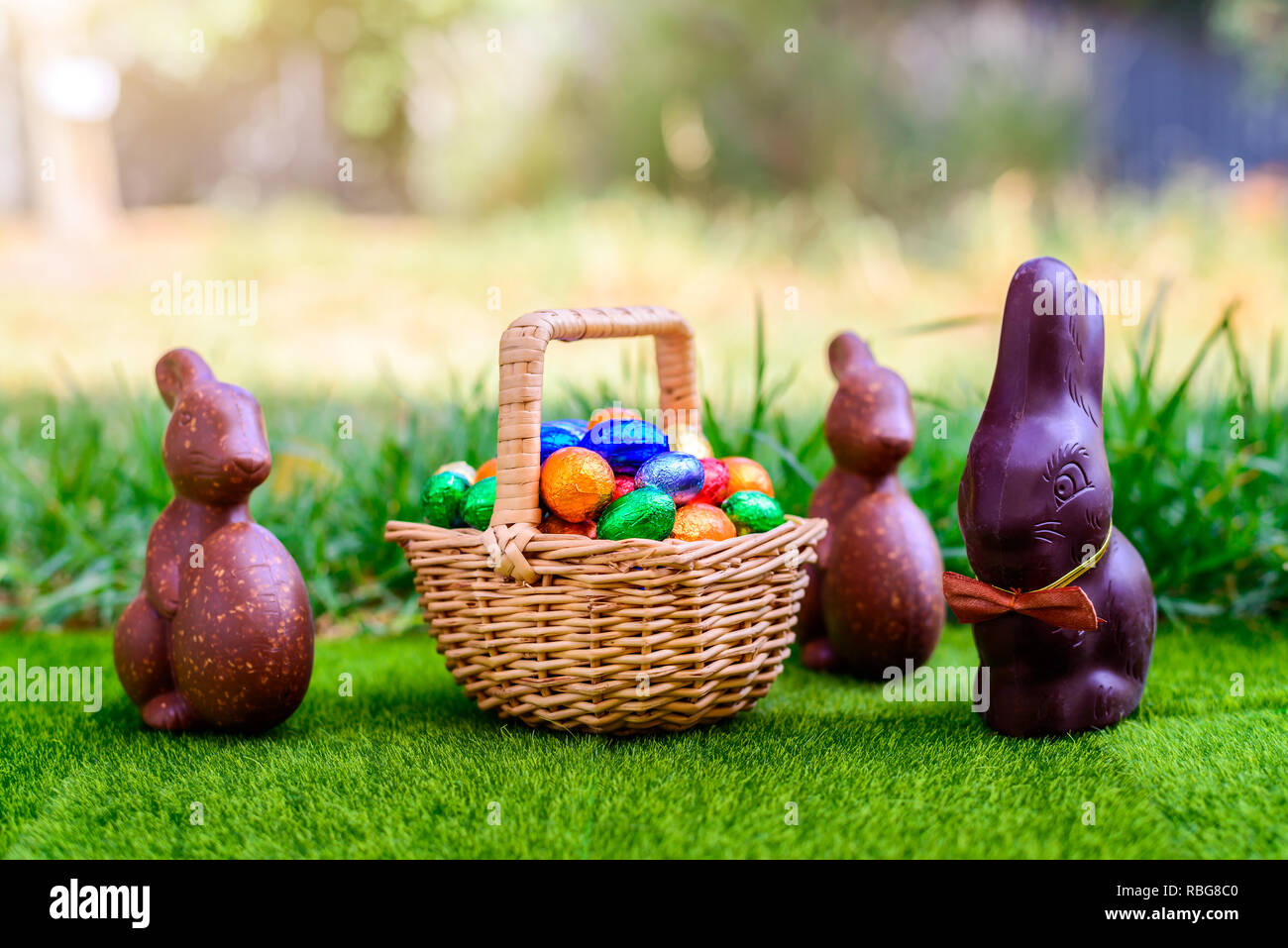 Schokolade Osterhasen mit Stroh Korb voll bunter Eier auf grünem Gras Hintergrund Stockfoto