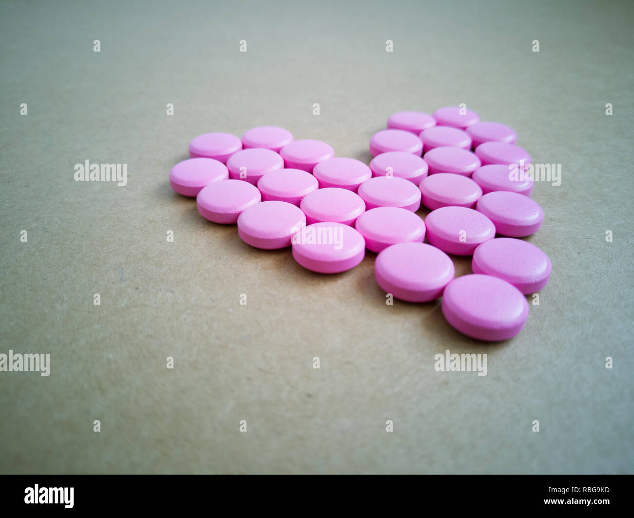 Rosa Pillen in Form eines Herzens auf braunem Hintergrund. farbige Drogen. Konzept - Herz-Krankheit, Herz-Kreislauf-Erkrankungen und Medikamente, Kardiologie, Valentine Stockfoto